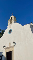 Fototapeta premium eautiful white church with blue accents on a beach, glistening under the sunlight with a clear blue sky. Perfect for travel, coastal architecture, Mediterranean charm, and serene landscapes