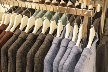 Obraz premium Warm knitted sweaters hang on white hangers in clothing store.
