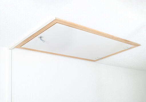 Closed attic hatch or loft door in ceiling. Attic door located in building staircase. Used to access a loft, storage space or attic. Selective focus.
