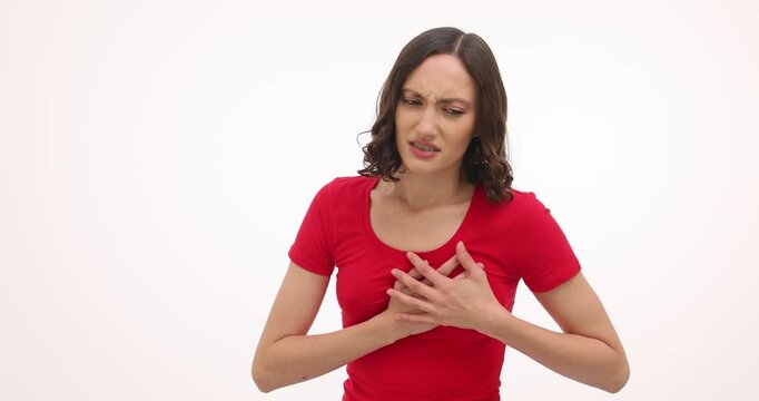 Young woman puts hands on chest feeling strong pain in heart on white background. Ill brunette female suffers from painful symptoms of heart attack