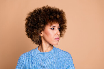 Photo of young funky american lady with brown hair chevelure in blue knitted sweater looking empty space isolated on beige color background