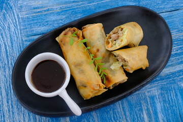 vegetable fried spring rolls in a black plate on a blue table. soy sauce near the spring rolls. lumpia. 