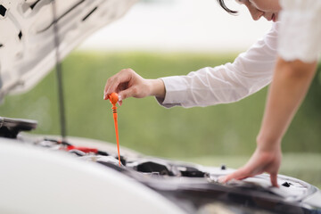 Checking the Oil: A woman carefully checks the oil level in her car, demonstrating routine maintenance and car care.  
