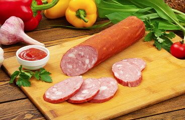 Sausage sliced ​​on a wooden board, against the background of fresh vegetables.