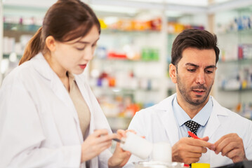 Fototapeta premium Pharmacists counting drug pills arranging assortment working in drug shelves counter