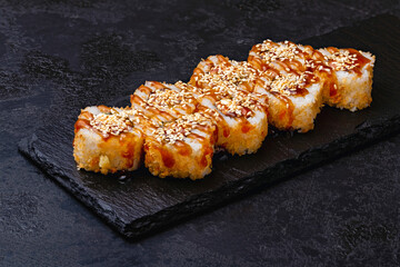 Japanese sushi, fried tempura rolls with unagi sauce and sesame on a black background