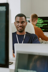 Vertical shot of young African American man coding or programming at work in modern IT company office