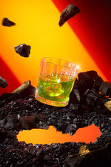 A glass of yellow cocktail floating suspended in the middle on a pebbles ring, with charcoal...