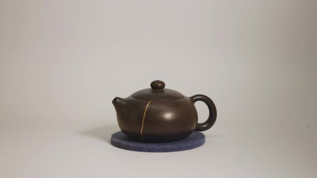 Ceramic Tea pot with a kintsugi repair gold crack on a felt pad with a white background.
