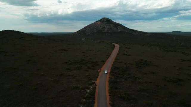 aerial shot over hellfire road in Cape Legrand National Park with a van driving on a dirt road to hellfire bay with the frenchman peak in the background on a cloudy day in Western Australia