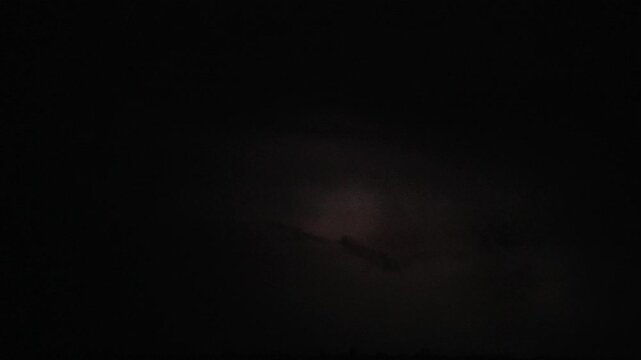 Heavy thunderstorm clouds with lightning strikes in the night sky.