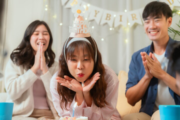 A group of friends sing and blow out candles at a birthday party at home.