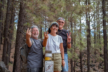 Happy group of senior friends enjoying vacation and adventure trekking in the forest, two elderly men and one woman looking at camera smiling. Sport, freedom, healthy lifestyle concept