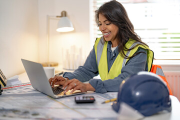 A construction professional collaborates on a project at her desk while reviewing plans and...