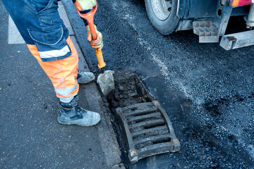 Worker repairing a drainage system on a busy city street during the early morning hours in a...