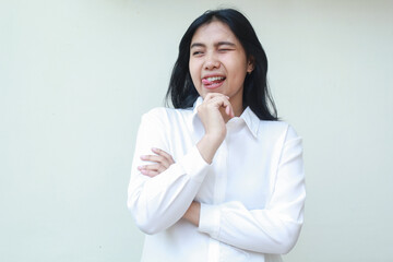 playful asian young business woman blink eye flirting aside thinking idea with hands on chin arms folded wearing white formal suit shirt, imagine plan with excitement, standing isolated background