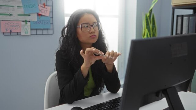 Woman working at computer in office thinking deeply wearing glasses and black blazer near strategy board and plant