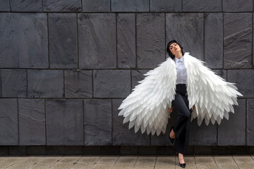A fashion model showcases stunning wing-inspired attire against a textured stone background in a...