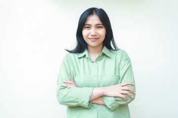 Fototapeta premium pleased successful dark hair asian woman wearing green over size shirt cross hands and looking at camera with confident face expression standing over isolated white background