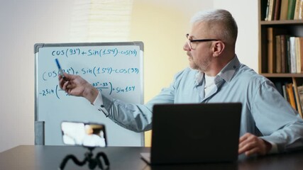 A teacher demonstrates math equations while conducting an online class from his workspace at home.