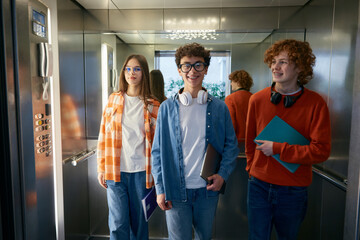 Three teenagers standing inside the elevator holding folder with papers © Nomad_Soul