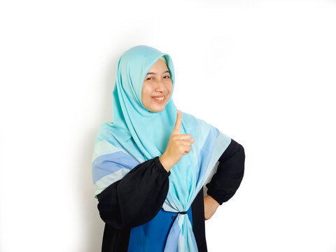 East asian indonesian muslim woman with hijab gamis smiling pointing finger to copy space isolated on blue background.
