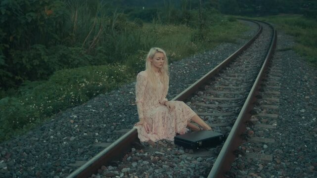 A woman sits along the railway tracks in a beautiful and peaceful landscape, enjoying the splendour of nature