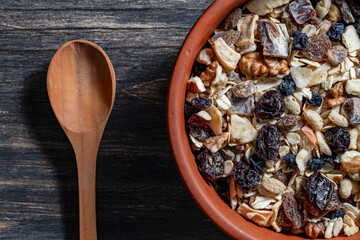 Whole grain oat muesli with dried fruits, nuts, raisins and berries in clay bowl on wooden table, top view, closeup. Background of organic muesli for breakfast