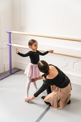 Obraz premium Cute little girl learning ballet from her experienced trainer in studio