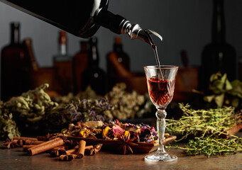 Brown herbal liquor or balm is poured from a vintage bottle into a glass.
