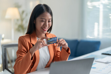Obraz premium Businesswoman is holding a credit card while working in her bright and modern office. She is shopping online using her laptop computer