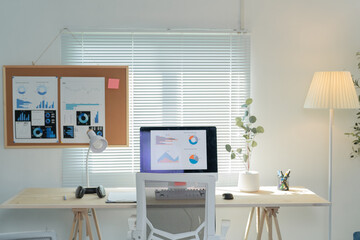 Brightly lit home office with a computer displaying analytics on the screen and a corkboard with additional charts and graphs