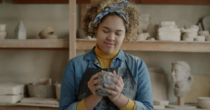Happy African American woman in apron working with clay in pottery workshop enjoying creative activity. Traditional art and earthenware concept.