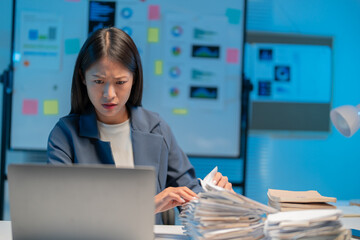 Businesswoman is feeling the pressure of a deadline as she works late into the night, searching...