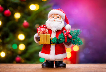 Obraz premium Santa Claus figurine holding a gift and a fir branch with Christmas lights bokeh background.