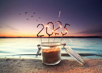 opened glass on the beach in the sunset with burning sparklers in the shape of the new year 2025	
