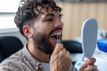 Man with metal braces carefully cleaning his teeth using interdental brush