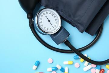 Blood pressure measuring device and pills on light blue background, top view