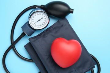 Blood pressure measuring device and squeeze heart on light blue background, top view
