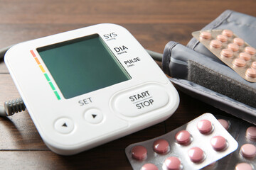 Blood pressure measuring device and pills on wooden table, closeup