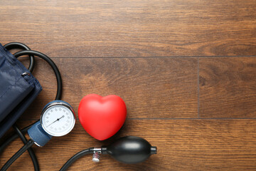 Blood pressure measuring device and squeeze heart on wooden table, top view. Space for text