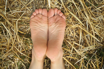 Woman lying barefoot on straw outdoors, top view