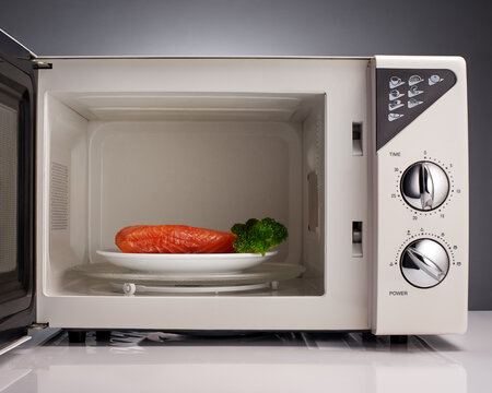 Salmon and broccoli on white plate in open microwave