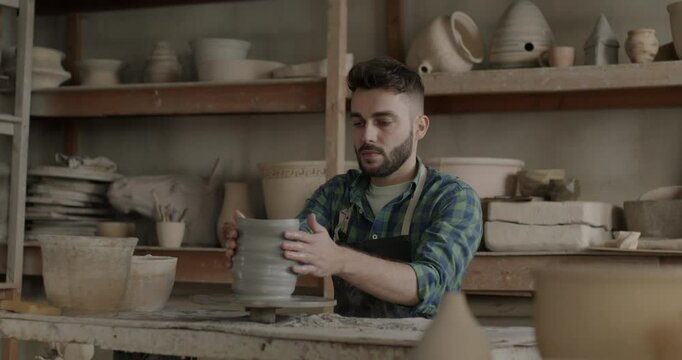 Slow motion portrait of young man making vase using pottery wheel concentrated on creative activity in workplace. People and small business concept.