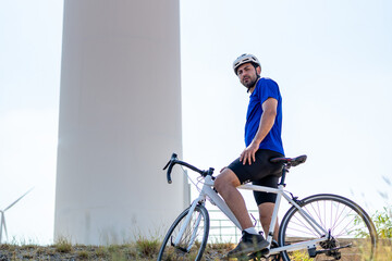 Obraz premium Portrait of Caucasian sportsman riding bicycle at wind turbine field. 