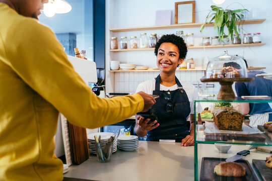 Bakery, happy portrait of black woman in cafe ready for serving pastry, coffee and baked foods. Restaurant, coffee shop and confident waiter barista by counter for service, help and welcome