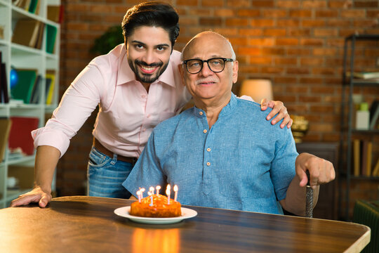 Indian son celebrating his elderly father’s birthday with cake, candle at home, joyful moments