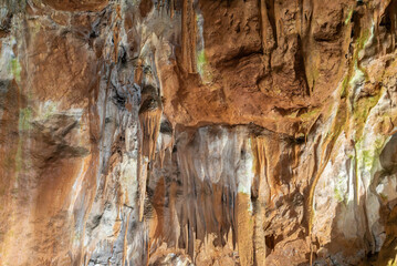 A rock wall with a lot of moss and some green spots. The wall is brown and has a lot of texture.