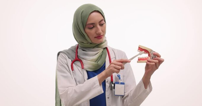 Muslim woman doctor shows technique for brushing teeth. Female dentist in hijab demonstrates proper dental care method using plastic model