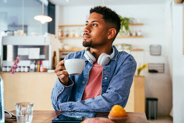 Handsome young hispanic man sitting in a bar cafeteria -  heerful african-american male relaxing in a pastry bakery coffee shop